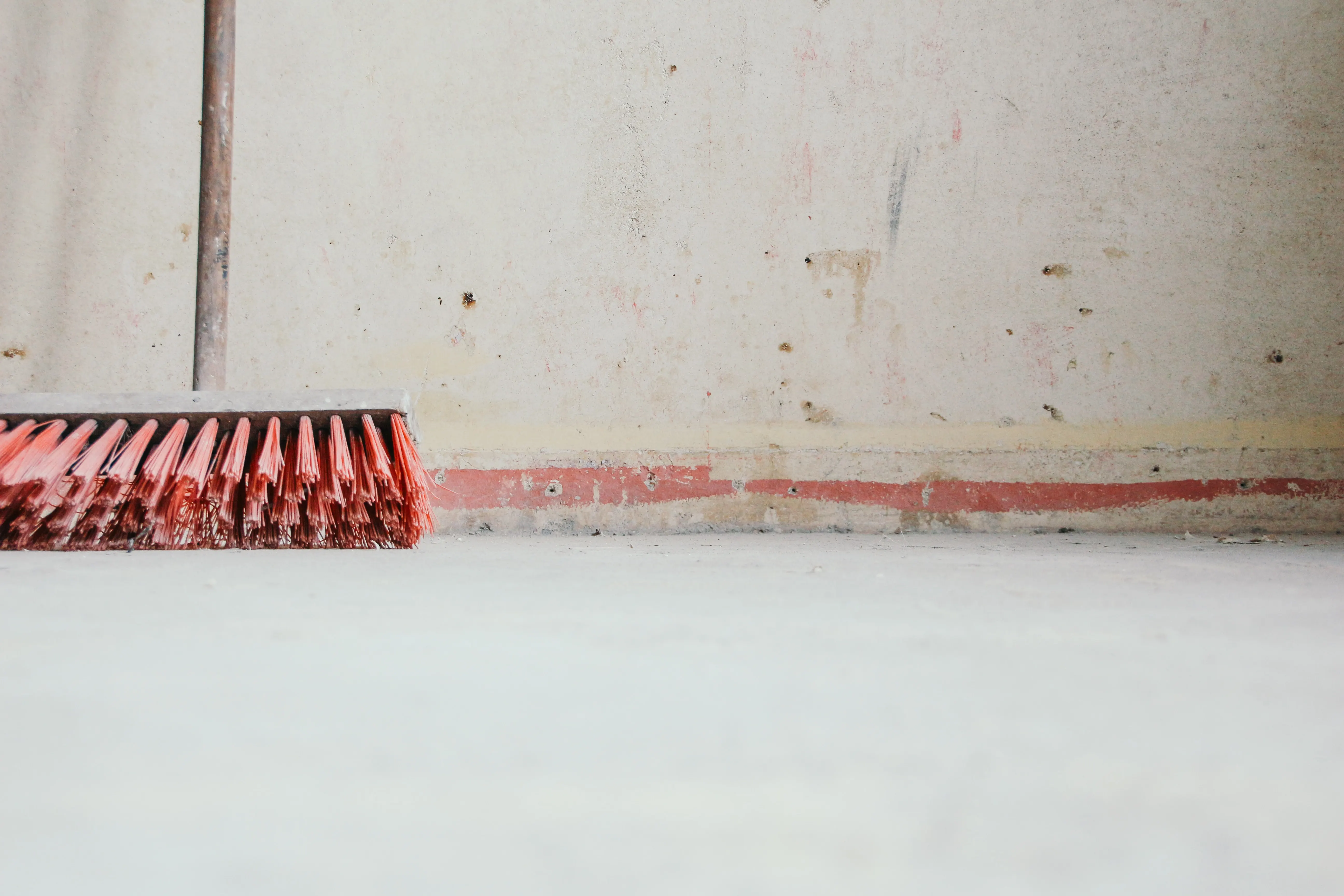 Red broom against a concrete wall