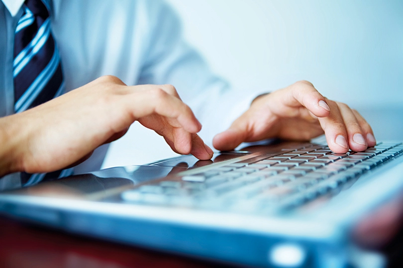 Person in a suit and tie typing on a laptop keyboard